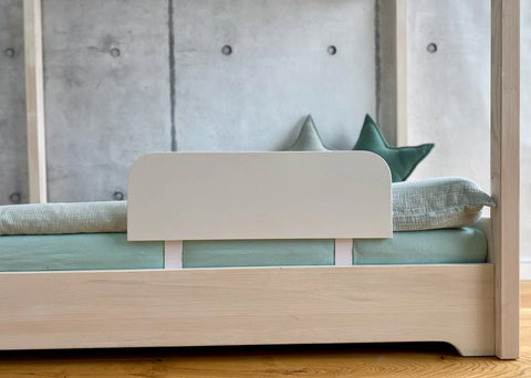 Ein minimalistisches Bett aus hellem Holz mit einer hellgrünen Matratze und Bettzeug, das an einer Betonwand steht. Zwei grüne Kissen sind am Kopfende des Bettes angebracht.