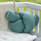 Eine Wickeltischrolle Musselin nilblau von KraftKids GmbH ruht auf einer weißen Kunstfelldecke, die über eine weiße Bank mit grauer Polsterung drapiert ist, im Freien mit verschwommenem Grün im Hintergrund.