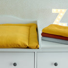 Eine weiße Kommode mit Schubladen enthält eine KraftKids Wickelauflage Doppelkrepp Gelb Senf und einen Stapel gefalteter gelber, roter und grauer Handtücher. Dahinter ziert ein beleuchteter Buchstabe Z eine hell getupfte Wand.