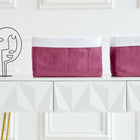 Auf einem weißen Tisch mit goldenen Beinen stehen zwei magentafarbene Körbchen Leinen von KraftKids und eine minimalistische schwarze abstrakte Gesichtsskulptur vor einer weiß getäfelten Wand.