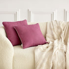 Ein cremefarbenes Struktursofa mit zwei Kissenbezügen Leinen magenta dunkel von KraftKids und einer beigefarbenen Struktudecke, die über die Seite drapiert ist, steht vor einer weißen Wand mit Zierleisten.