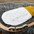 Ein KraftKids Strampelsack Frühling Sommer Musselin gelbe Zitronen liegt auf einem grauen Kunstfellteppich mit weißem Untergrund, gelber Spitze und Zitronenaufdrucken. Vorne auf dem Teppich sind eine Spielzeugeisenbahn aus Holz und eine gebogene Schiene platziert.