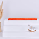 Ein weißes dreistufiges Podest mit einer KraftKids GmbH Sitzauflage für Ikea TROFAST Cord Breitcord Orange Reinorange auf der obersten Stufe steht zwischen einer beigen geflochtenen Vase mit Pampasgras (links) und einem kleinen weißen Holzschaukelpferd (rechts).