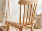Das KraftKids Sitzkissen für Stühle aus Musselin in zartem Rosa mit Blumenmuster und Schleife ist ein leichter Holzstuhl mit vertikalen Latten. Sein abnehmbarer Bezug bietet Komfort in dem gemütlichen, neutral getönten Raum.