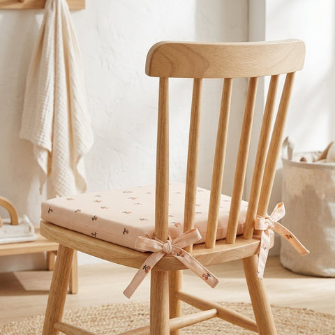 Das KraftKids Sitzkissen für Stühle aus Musselin in zartem Rosa mit Blumenmuster und Schleife ist ein leichter Holzstuhl mit vertikalen Latten. Sein abnehmbarer Bezug bietet Komfort in dem gemütlichen, neutral getönten Raum.