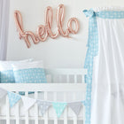Ein weißes Babybett mit blau-weißer Bettwäsche aus 100 % Baumwolle, einem handgefertigten Betthimmel "Weiße Pfeile auf Blau" von KraftKids und einem pastellfarbenen Wimpel-Banner. Oben prangen roségoldene "Hallo"-Ballons vor einer weißen Wand - ideal für ein Himmelbett-Kinderzimmer.