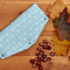 Der KraftKids Kinderwagenmuff weiße Pfeile auf Blau, ein hellblauer Fleece mit weißem Pfeilmuster und Metalldruckknöpfen, liegt auf Holz inmitten von Herbstblättern und Kastanien - ideal, um die Hände an kühlen Tagen warm zu halten.