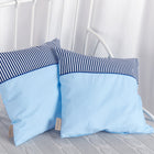 Zwei KraftKids Kissenbezüge "weiße Punkte auf Hellblau, Streifen dunkelblau" liegen auf einer hellgrauen, strukturierten Decke auf einem weißen Metallbettgestell, mit weißen Gardinen im Hintergrund.