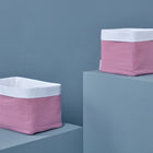 Zwei rosa KraftKids Körbchen Musselin rosa mit weißen Rändern stehen auf hellblauen Podesten. Ein Korb ist erhöht, der andere ist niedriger - eine ideale Ablage für die wichtigsten Dinge auf dem Wickeltisch.