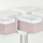 Zwei rechteckige KraftKids Körbchen Musselin goldene Punkte auf Rosa mit hellrosa Seiten und weißen umgeschlagenen Rändern, ideal für die Aufbewahrung auf dem Wickeltisch, werden auf weißen geometrischen Blöcken vor weißem Hintergrund dargestellt.