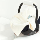 Die KraftKids Decke für Babyschale Winter Musselin mit goldenen Punkten auf Weiß liegt über einer schwarzen Babyschale, inszeniert auf weißen geometrischen Plattformen im minimalistischen Stil.