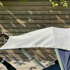 Das luftdurchlässige KraftKids Sonnensegel Musselin goldene Punkte auf Weiß bedeckt das Verdeck eines blauen Kinderwagens mit braunem Griff, der draußen vor einer Holzwand im Sonnenlicht steht.