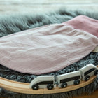 Ein KraftKids Strampelsack Frühling Sommer Doppelkrepp Rosa Babyschlafsack liegt auf einem flauschigen grauen Teppich, um den herum ein hölzerner Spielzeugeisenbahnzug auf einer hölzernen Eisenbahnschiene kreist.