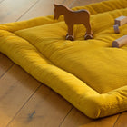 Die KraftKids Krabbeldecke Doppelkrepp Gelb Senf aus Polyestervlies ruht auf einem Holzboden, auf dem ein Spielzeugpferd und Bauklötze stehen, während das Sonnenlicht die gemütliche Szene erhellt.