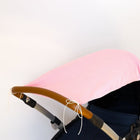 Ein Kinderwagen mit braunem Griff und dunklem Stoff hat das KraftKids Sonnensegel weiße Punkte auf Koralrosa, das mit weißen Bändern am Verdeck befestigt ist. Der Hintergrund ist einfarbig weiß.