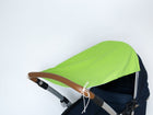 Ein KraftKids Sonnensegel weiße Punkte auf Grün mit weißen Schnüren bedeckt einen Kinderwagen mit dunklem Sitz und braunem Griff, der vor einem einfarbig weißen Hintergrund abgebildet ist.
