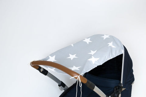 Der KraftKids Sonnensegel große weiße Sterne auf Grau ist ein hellgraues Kinderwagenverdeck mit großen weißen Sternen, hergestellt aus atmungsaktiver Baumwolle. Abgebildet auf einem Kinderwagen mit braunem Griff und dunkelmarinefarbenem Sitz vor einem schlichten weißen Hintergrund.