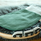 Ein KraftKids Strampelsack Herbst Winter Doppelkrepp Grün Jade liegt auf einem grauen Kunstfellteppich neben einer geschwungenen Holzeisenbahnstrecke mit einer kleinen schwarz-weißen Spielzeugeisenbahn.