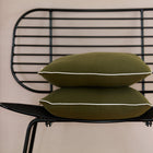 Zwei KraftKids Kissenbezug Doppelkrepp Grün Herbstgrün sind auf einem modernen schwarzen Drahtstuhl vor einer hellbeigen Wand gestapelt - ideal, um sie mit Ihrer Lieblingsbettwäschekollektion zu kombinieren.