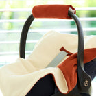 Eine Nahaufnahme der KraftKids Decke für Babyschale Winter Doppelkrepp Rot Herbstrot mit cremefarbenen und orangefarbenen Akzenten, die in einem Raum in der Nähe eines Fensters platziert wurde, in dem das Sonnenlicht durch horizontale Jalousien fällt.