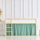 In einem minimalistischen Kinderbett steht das KraftKids Hochbettvorhänge Set 2+1 Doppelkrepp Grün Jade für das Kura Bett vor einer weiß getäfelten Wand. Eine geflochtene Vase mit Pampasgras und zwei Holzhocker stehen auf dem hellen Boden.